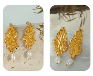 Close-up of golden leaf earrings with freshwater pearls on a natural stone base