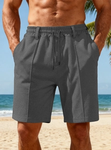 Detail of grey men's waffle knit beach shorts featuring drawstring waist on beach background