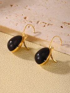 Detailed view of teardrop resin earrings with gold base on stone textured background