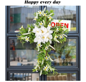 Detail of cross-shaped Easter wreath with white lilies and green leaves on glass door