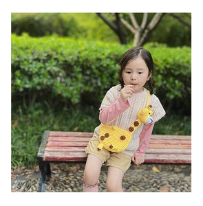 Outdoor shot of a toddler girl wearing a cute yellow knitted giraffe crossbody bag
