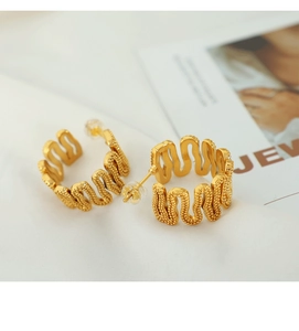 Macro detail of gold C-shape wave earrings with beaded texture on white silk fabric