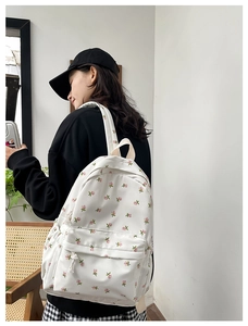 Detail of white floral backpack with pink roses and beige straps in a cafe setting