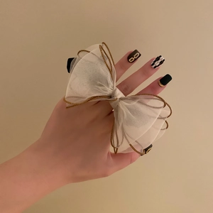Macro detail of cream organza hair scrunchie with gold trim on a hand with nail art