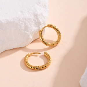 Detail showing golden hoop earrings with geometric embossed texture and latch closure