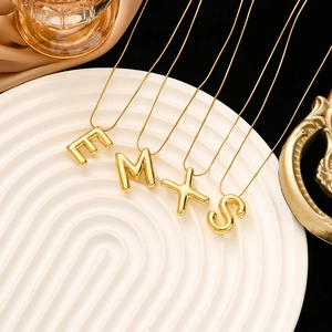 Detail of 3D gold balloon letter pendants E M X S on snake chains with luxury background