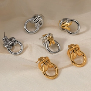 Interlocking twist knot hoop earrings in gold and silver finishes on beige velvet
