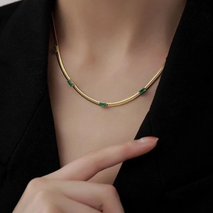 Elegante collana a serpente dorata con zirconi verde smeraldo rettangolari su una modella