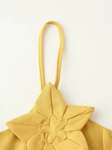 Détail macro d'une robe jaune en tissu tissé avec décoration florale 3D sur l'épaule