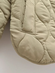 Detail of light khaki quilted jacket showing wave stitching and hidden side pockets