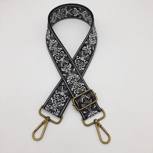 Adjustable wide embroidered bag strap with ethnic pattern and brass hardware on white background