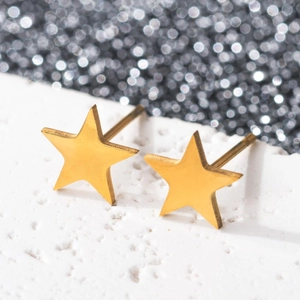 Macro shot of gold star stud earrings with brushed metal finish on textured stone