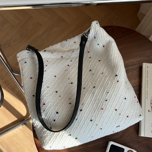 White tweed tote bag with colorful specks and black leather straps on a wooden table