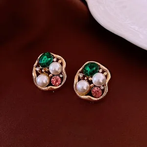 Vintage irregular gold earrings with emerald gemstones and white pearls on velvet