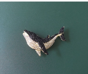 Macro shot of whale brooch featuring black and white crystals on a gold-toned base