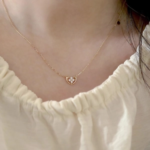 Close-up of golden heart pendant with zircon four-leaf clover on a female neckline