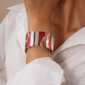Close-up of geometric enamel bracelet with red orange patterns and hammered metal finish