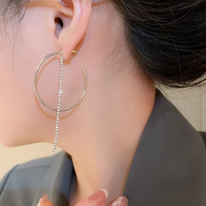 Dettaglio di orecchini a cerchio argento con lunghe nappe di strass indossati da una modella