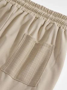 Detail of light beige casual trousers featuring elastic waist and plaid texture pocket design