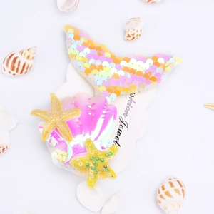Close-up of holographic mermaid tail and sequin starfish hair clips on a themed background