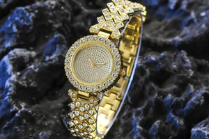 Close-up of luxury gold women's watch featuring crystal pavé dial and intertwined chain band