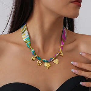 Detail of colorful printed silk ribbon necklace with gold heart-shaped charms on model