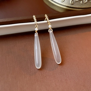 Macro detail of teardrop earring featuring white stone, pearls, and gold hooks