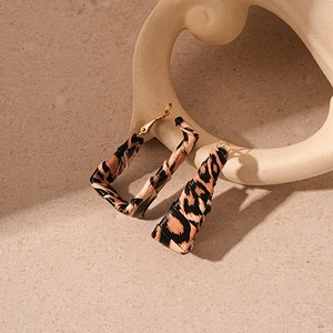 Close-up of geometric leopard print earrings with gold hooks on a beige artistic base