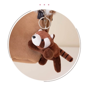 Close-up of a cute brown red panda plush keychain hanging on a stylish brown bag