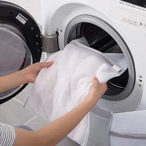 White fine mesh laundry bag with grey zipper being placed inside a washing machine