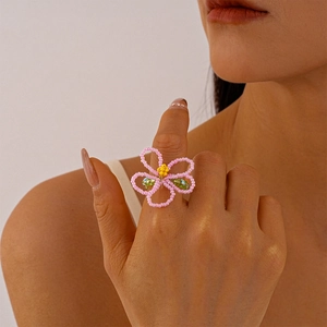 Detailed view of handmade pink glass flower bead ring with green leaves on model finger