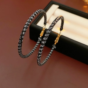 Detailed view of large black leather hoop earrings with white repeating letter pattern
