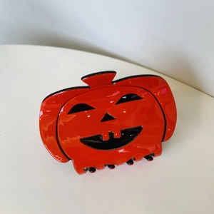 Close-up of bright orange pumpkin hair claw clip with black Jack-o'-lantern face