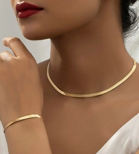 Detail of gold flat snake chain necklace and matching bracelet set on female model