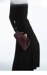 Detailed view of dark burgundy woven cloud clutch bag styled on a black dress