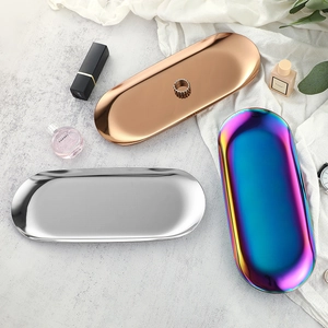 Oval stainless steel jewelry trays in gold, silver, and rainbow finishes on a textured table