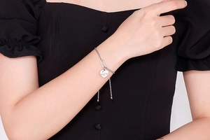 Close-up of a silver heart charm bracelet with adjustable chain on a woman wrist