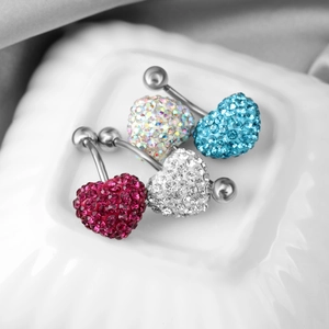 Set of four stainless steel heart navel rings with colorful crystals on a white ceramic plate