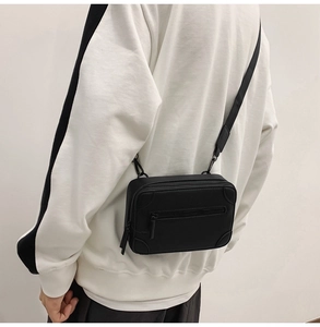 Detail of a black structured box crossbody bag featuring reinforced corners and leather texture