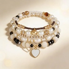 Vista detallada de pulsera multicapa con perlas, pedrería y colgantes de corazón