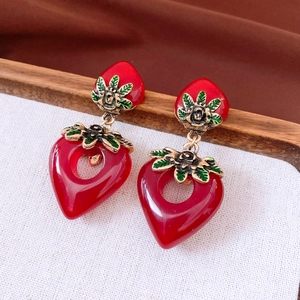 Detail of red heart strawberry earrings with golden floral accents on white linen