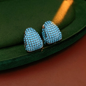 Close-up of C-shaped earrings with sky blue stones and silver metal finish