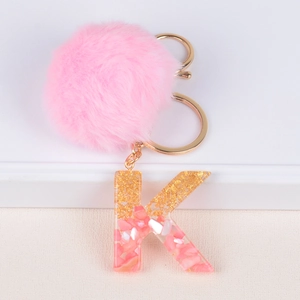 Detail of pink faux fur pompom and resin letter K keychain with gold foil flakes