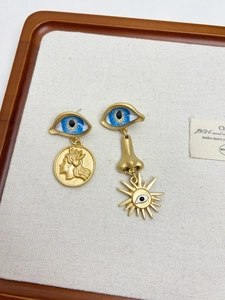 Detail of surrealist asymmetric matte gold earrings featuring blue eyes and coin relief