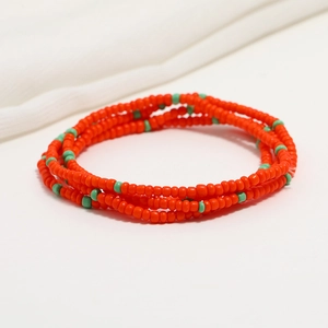 Detailed view of layered orange and turquoise seed bead body chain on white fabric