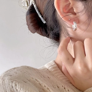 Close-up of minimalist silver C-shaped chunky hoop earrings worn by a model in soft light
