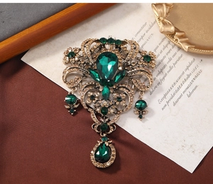 Close-up of vintage gold brooch with emerald crystals and teardrop pendant detail