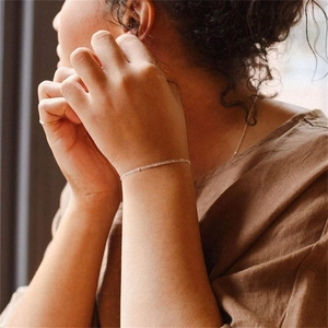 Detailed close-up of a minimalist silver chain bracelet on a model wearing brown linen