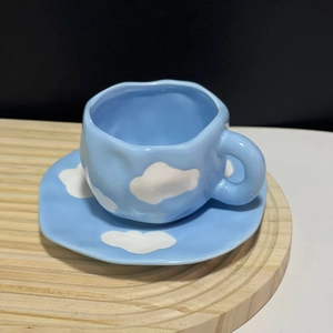 Detail of handmade irregular ceramic coffee cup with blue sky and white cloud pattern