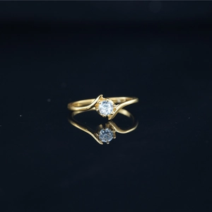 Elegant gold bypass moissanite ring with a brilliant round center stone on black mirror
